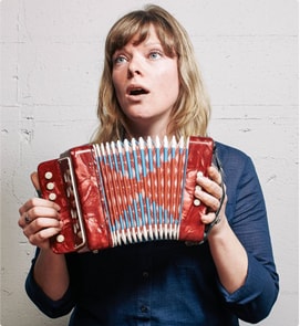 A woman holding an accordion in front of a white wall.