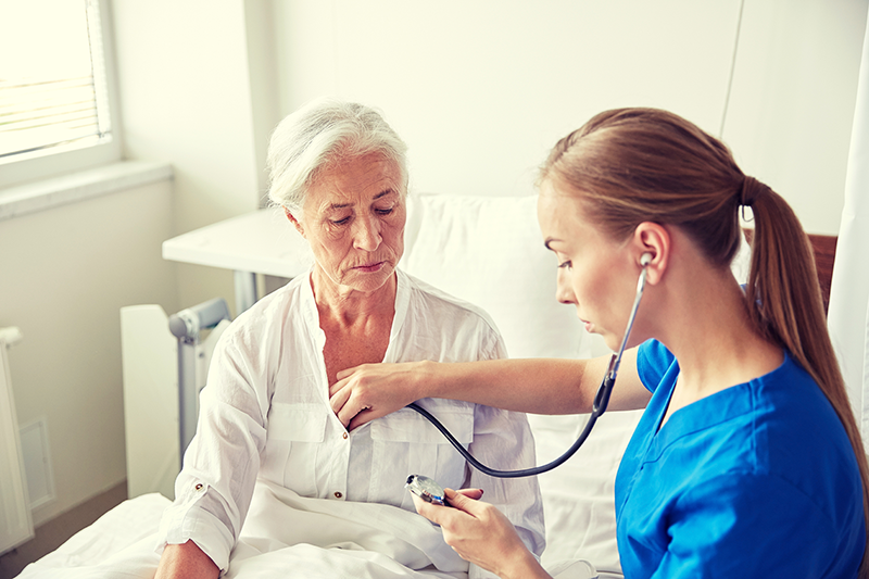 A nurse is taking a stethoscope to an elderly patient.
