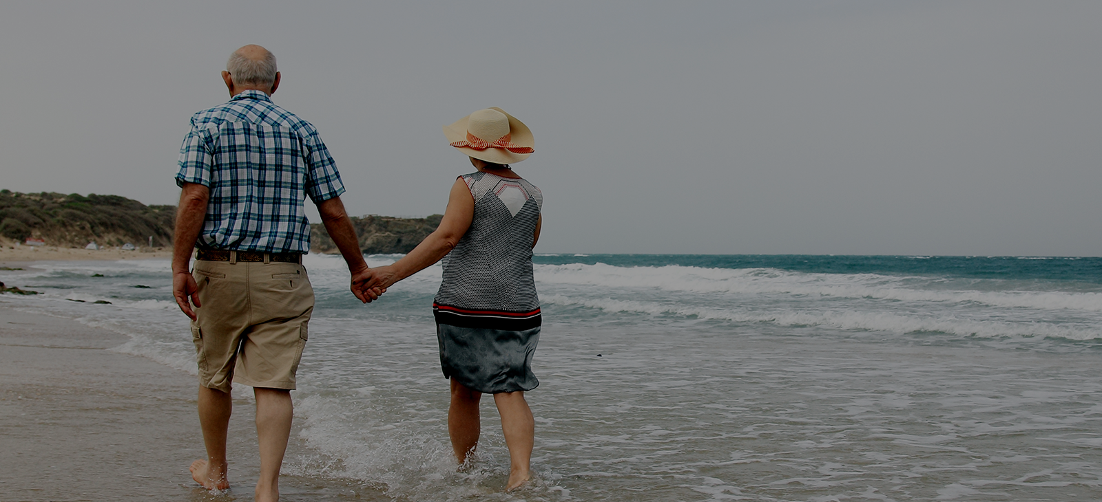 An older couple holding hands on the beach.