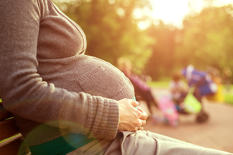 A pregnant woman sitting on a bench in a park.