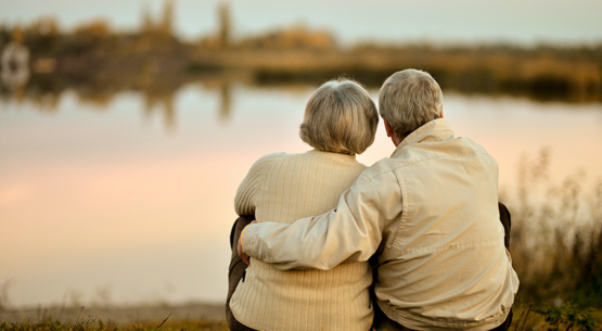 An older couple sitting on the grass looking at a lake.